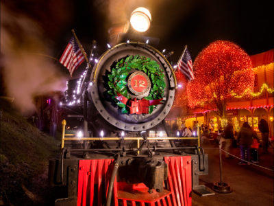 A steam locomotive decorated for Christmas with a wreath and Christmas lights.