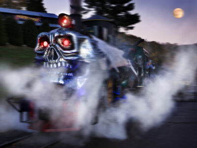 A steam locomotive with a skull face facade and red glowing eyes at night with a full moon